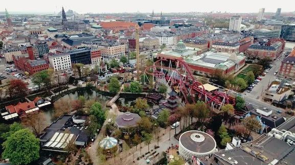 Billede af Tivoli-forlystelsesparken i København, oplyst med smukke lys, der skaber en magisk atmosfære. Forlystelser og gæster nyder den historiske og charmerende park.